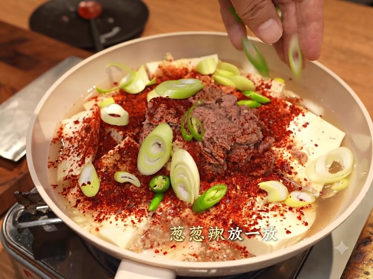 Hände streuen geschnittene Frühlingszwiebeln und grüne Chilischoten über die Pfanne.