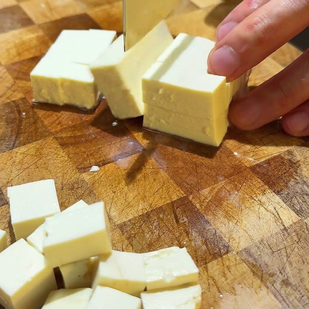 Seidentofu wird auf einer Holzschneidefläche in saubere kleine Würfel geschnitten.