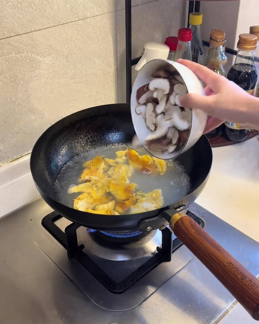 In Scheiben geschnittene Shiitake-Pilze werden in das kochende Wasser und Eiergemisch gegeben.