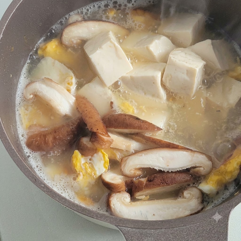 Würfel aus weichem weißem Tofu köcheln in einer herzhaften Brühe neben geschnittenen Pilzen und gebratenen Eierstücken.