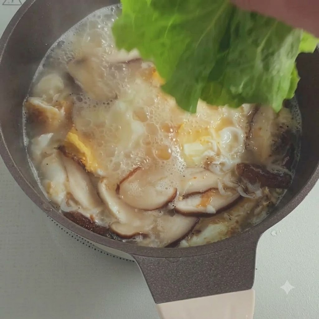 Frische Salatblätter werden in einen Topf mit blubbernder Suppe samt Pilzen und Eiern gegeben.