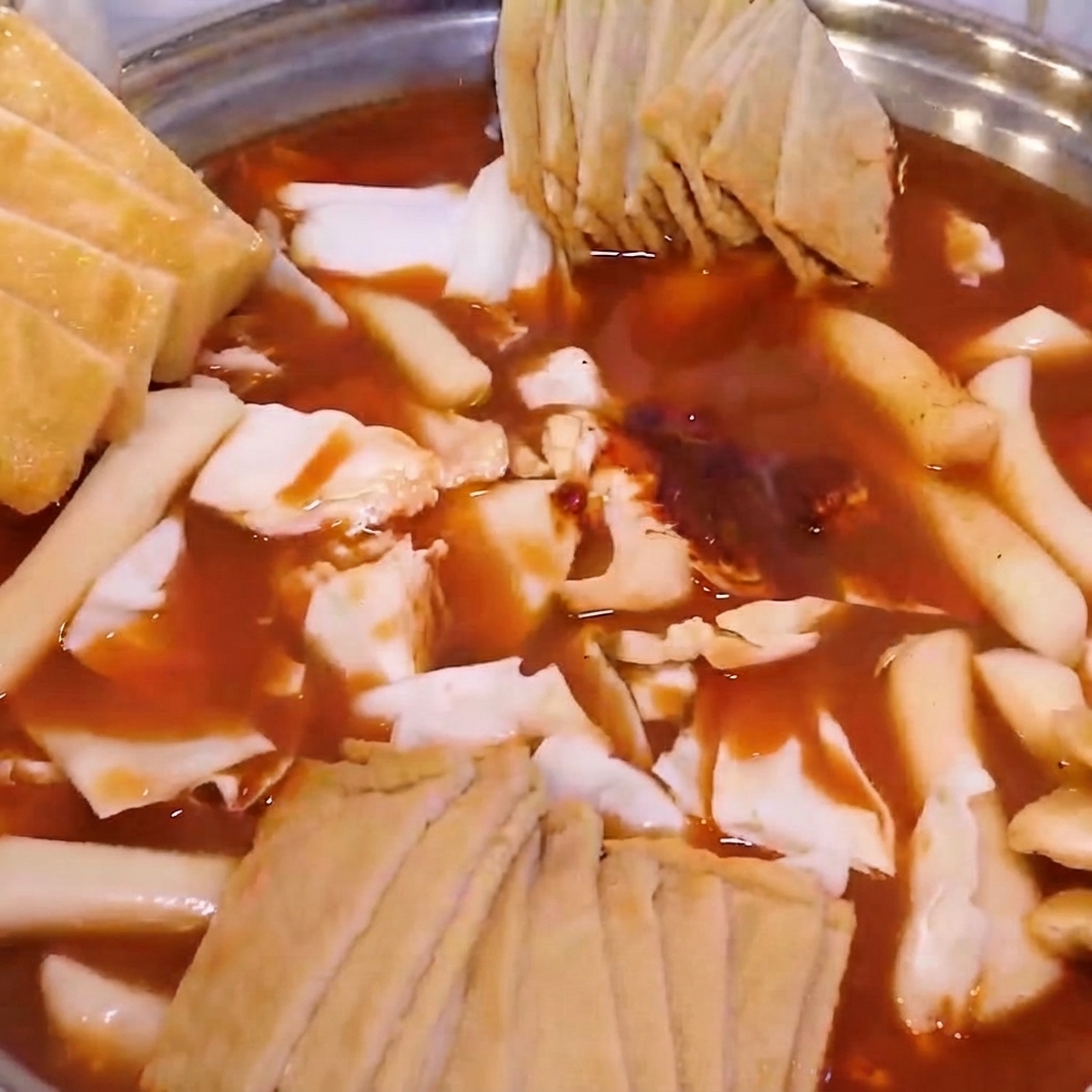 Ein mit Kohl, Reiskuchen und Fischkuchen gefüllter Hotpot, belegt mit frittiertem Tofu und Frühlingszwiebeln.
