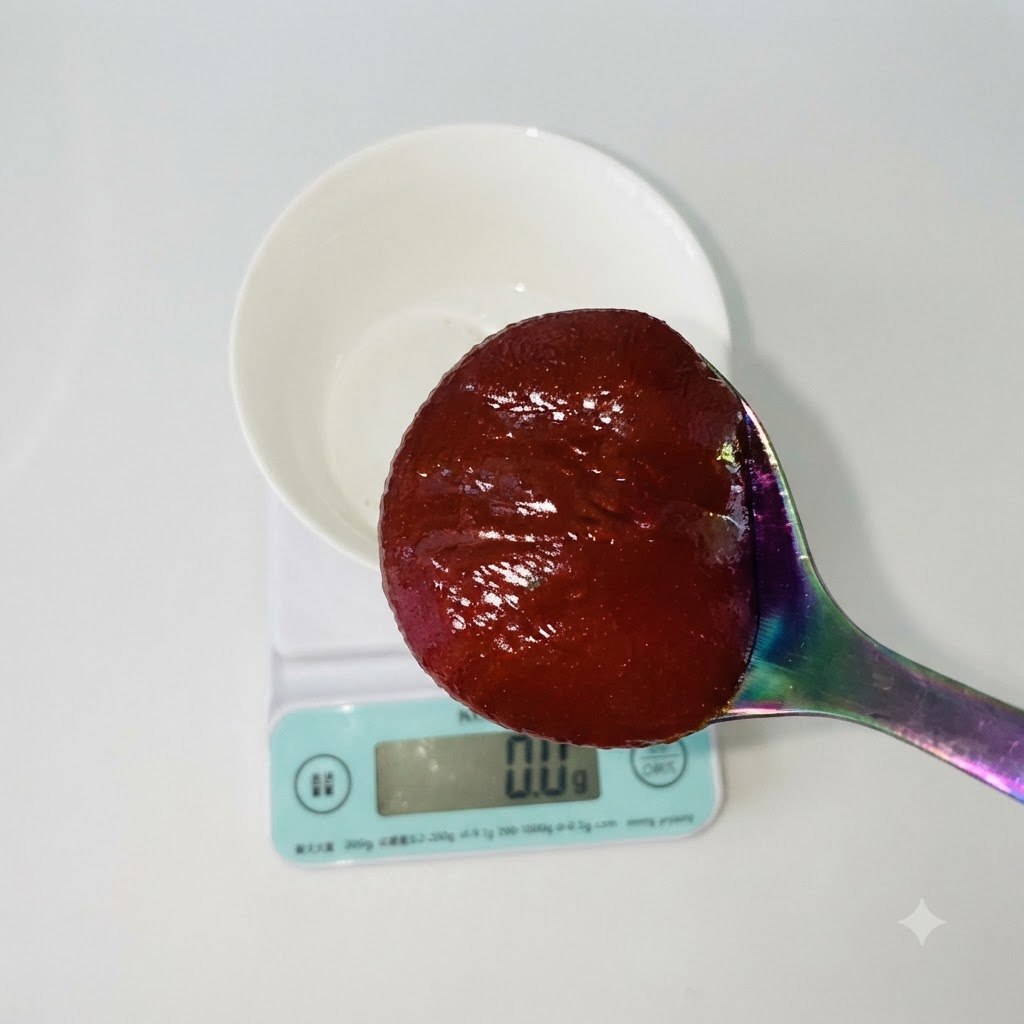 Ein Löffel roter koreanischer Chilipaste über einer weißen Schüssel auf einer digitalen Küchenwaage.