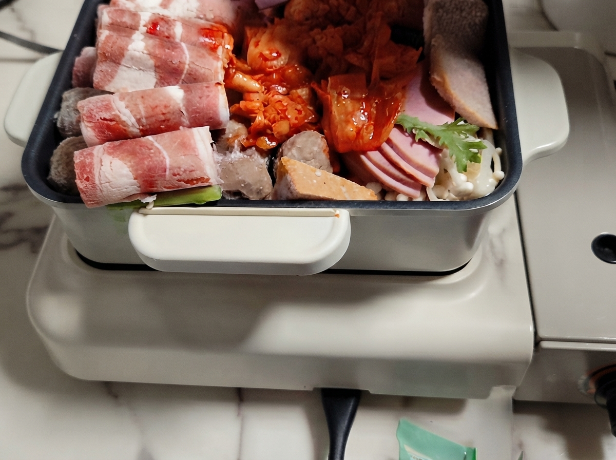 Ein heißer Pot gefüllt mit angeordneten Schichten aus Fleisch, Gemüse und Reiskuchen, über die Brühe gegossen wird.