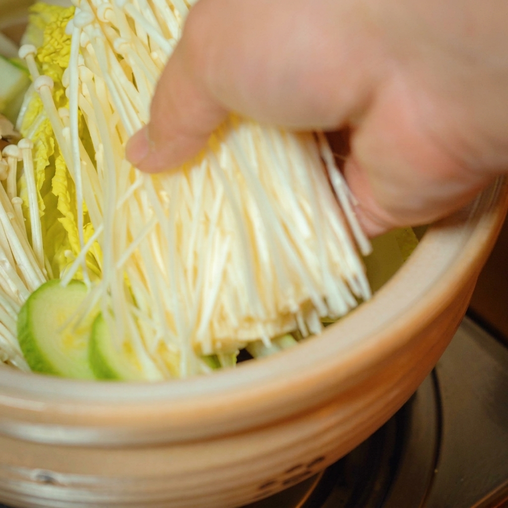 Frische Enoki-Pilze werden oben auf das Gemüse in den Topf gelegt.