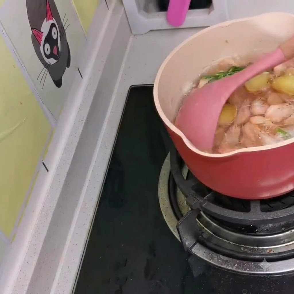 Kleine weiße Garnelen werden mit einem rosa Pfannenwender in einen köchelnden Topf mit koreanischen Ramen eingerührt.