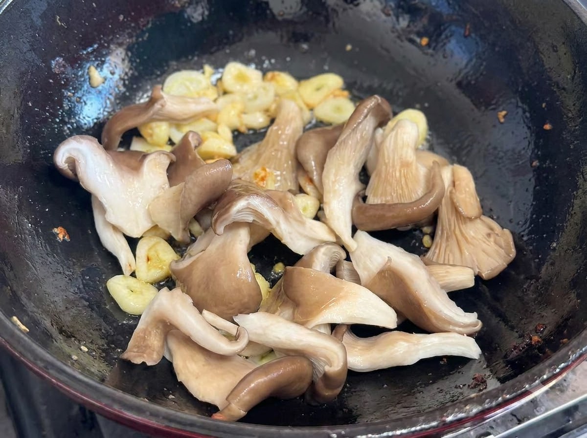 Frische Austernpilze werden mit Knoblauch und Frühlingszwiebeln in den Wok gegeben.