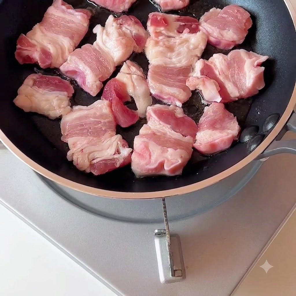 Schweinebauchscheiben brutzeln und bräunen in einer Pfanne.