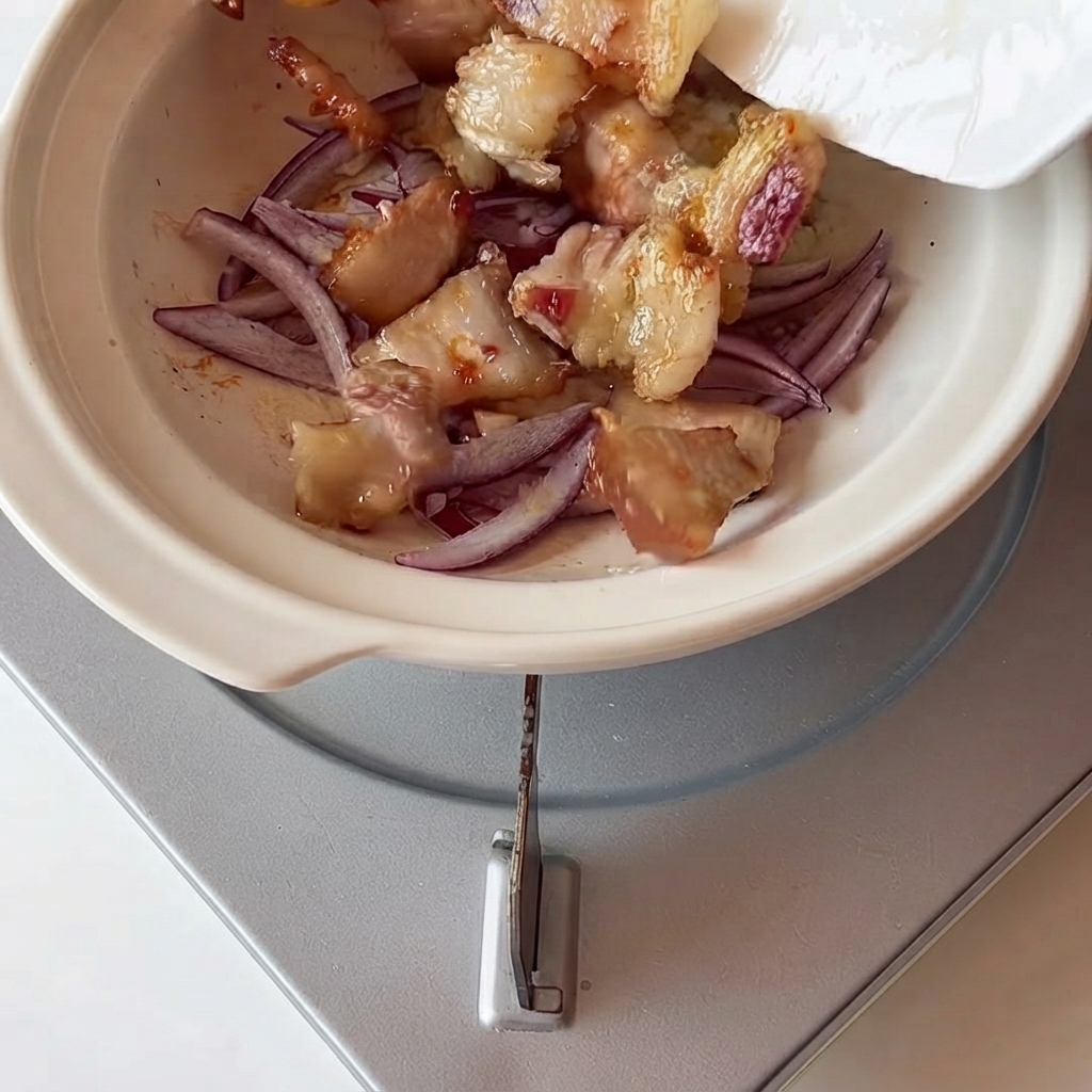 Schweinebauch und Kimchi werden mit Zwiebeln in einem Topf kombiniert.