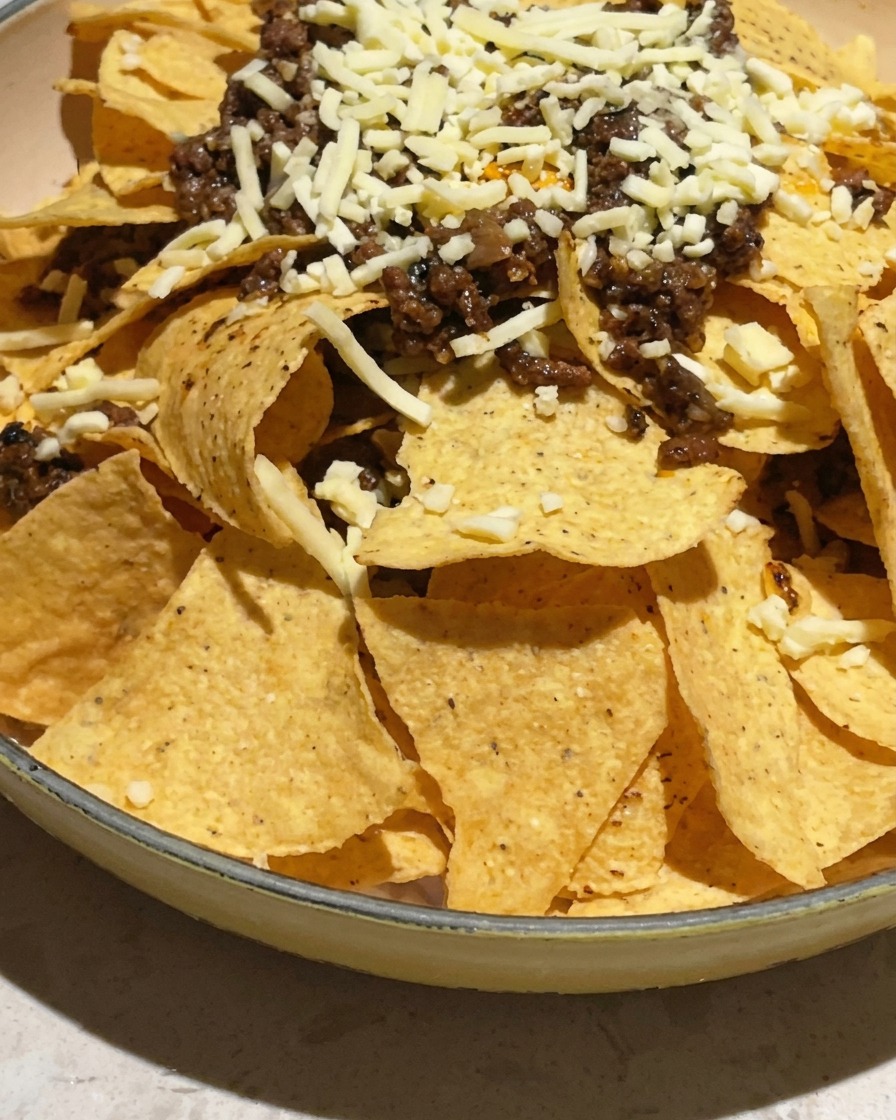 Mit Tortilla-Chips, Fleischsauce und geriebenem Käse gefüllte Backform, bereit für den Ofen.