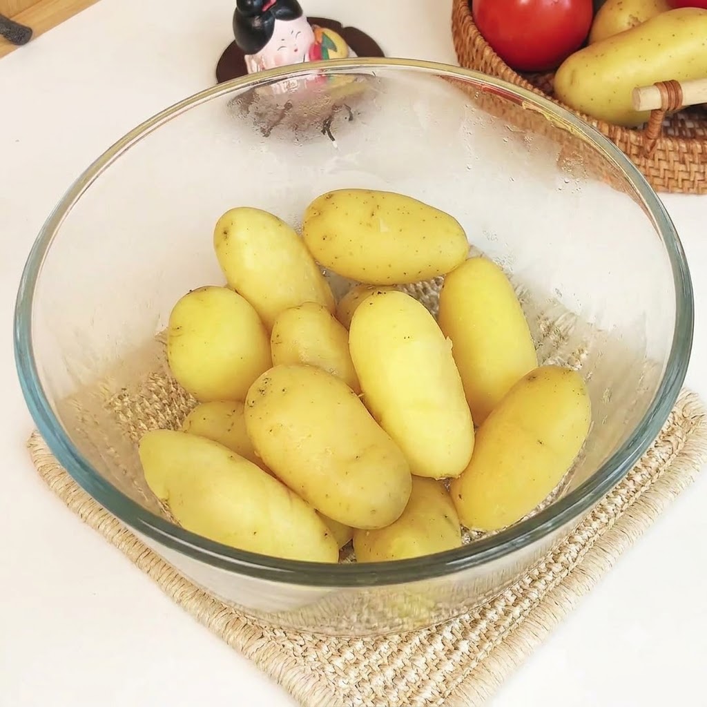Gedämpfte Kartoffeln in einer klaren Glasschüssel zusammen mit Butter und Käse, die zu einem glatten Püree gestampft werden.