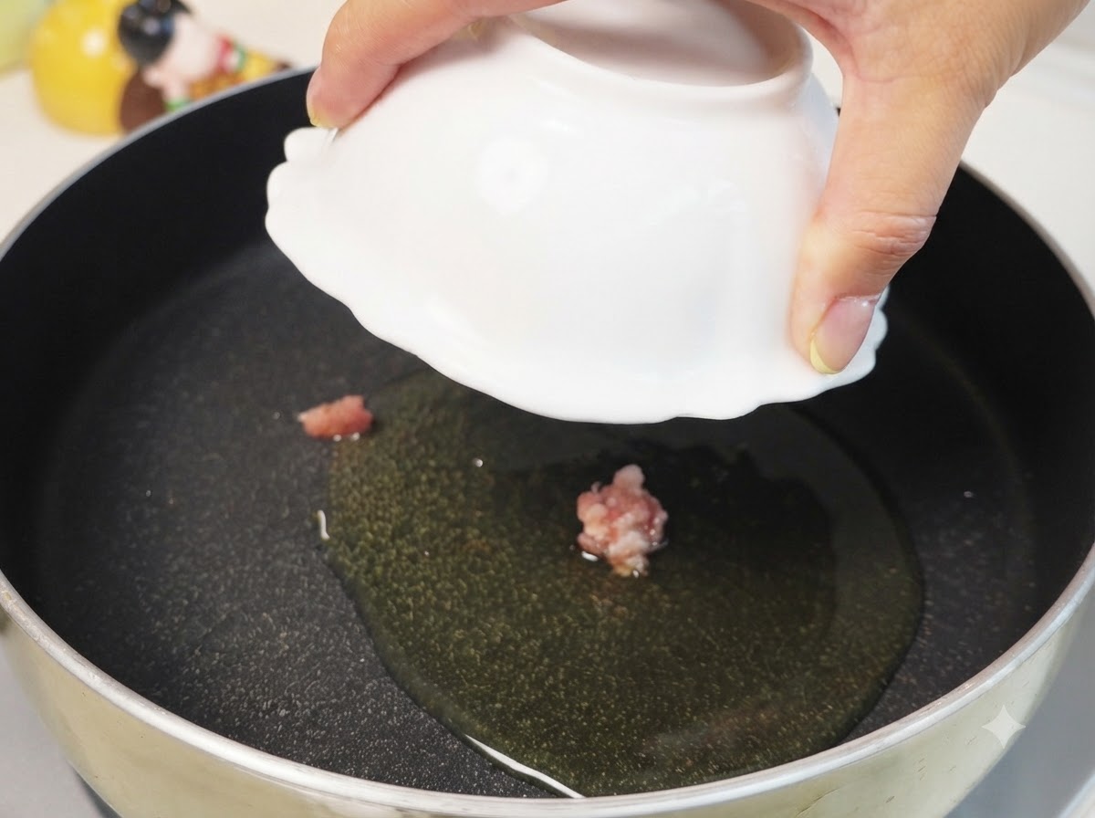 Schweinehackfleisch kocht in heißem Öl in einer schwarzen Pfanne bei mittlerer bis niedriger Hitze.