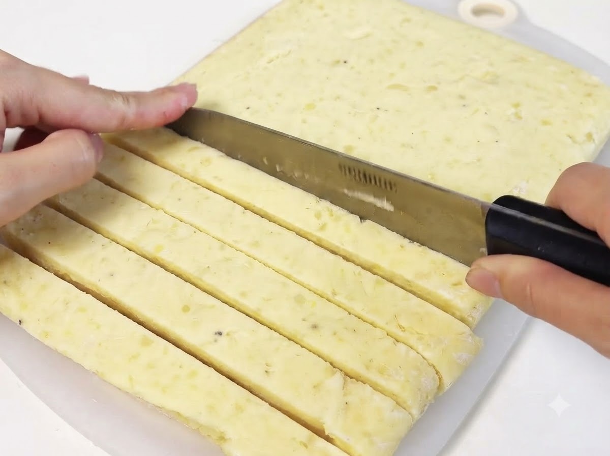 Ein Messer schneidet durch eine feste Platte gefrorenen Kartoffelpürees, um lange Streifen zu formen.