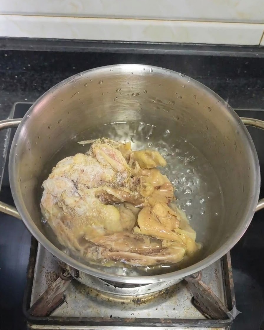Eine frische Scheibe Ingwer wird in einen köchelnden Topf mit Wasser und Hähnchenstücken gegeben.