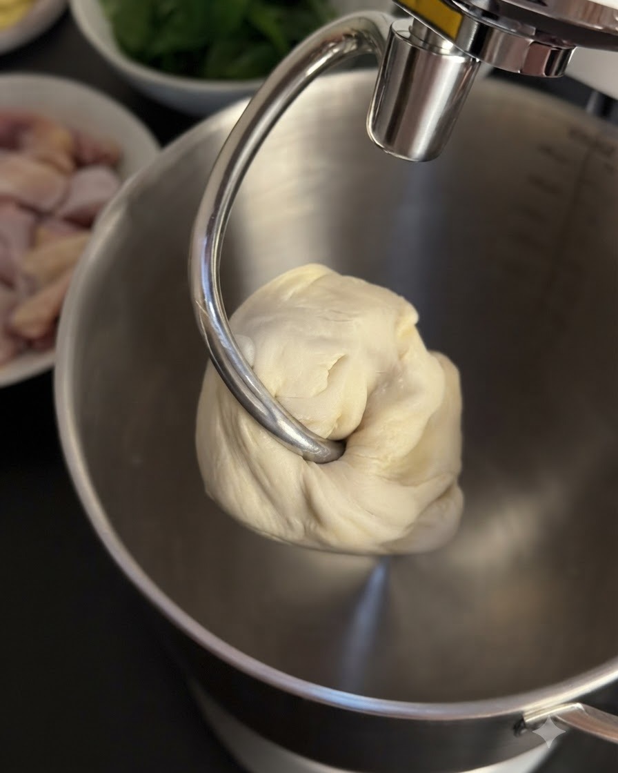 Eine Kugel gekneteter Teig hängt am Knethaken der Küchenmaschine.