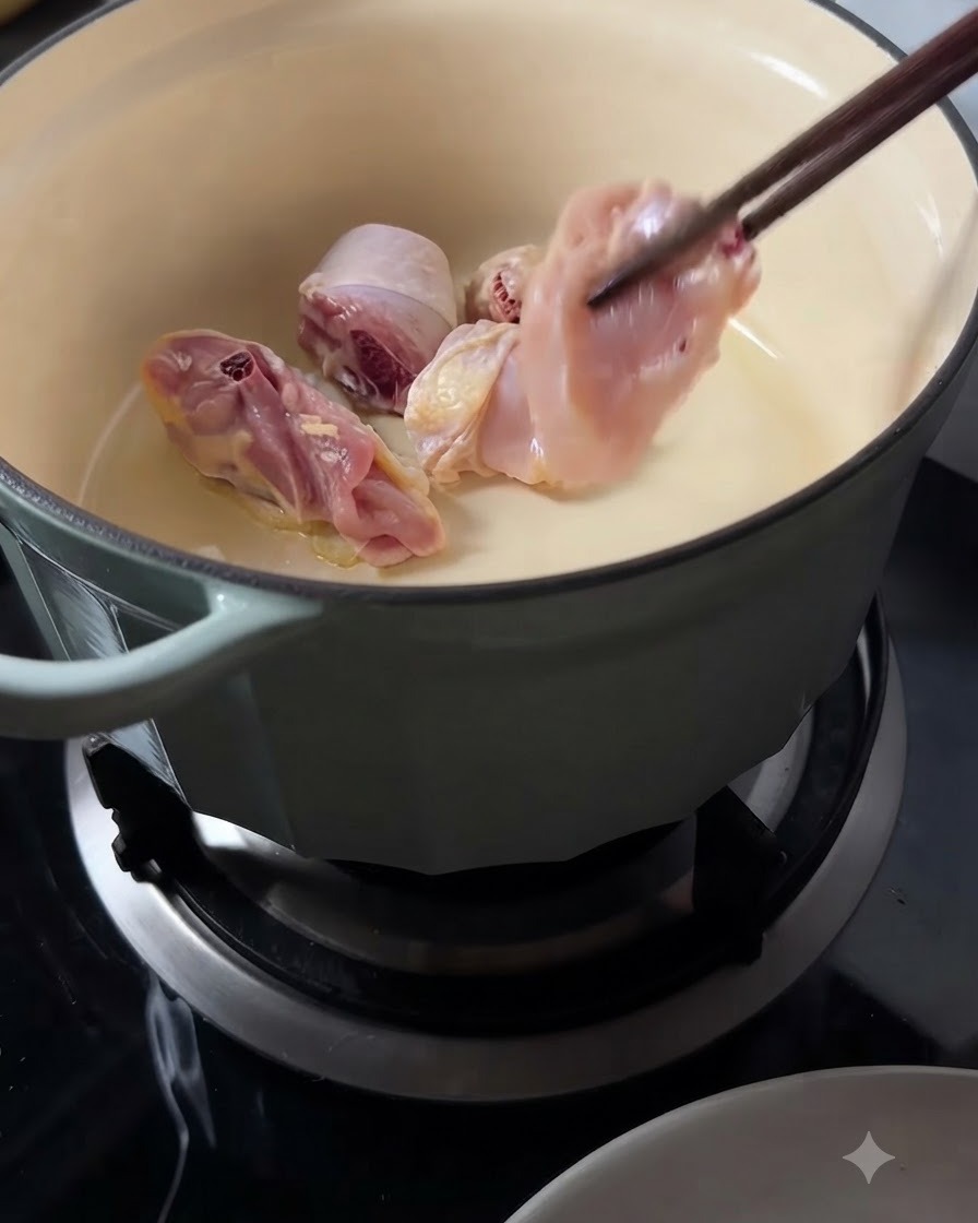 Rohe Hähnchenstücke werden mit langen Holzstäbchen in den heißen Topf gelegt.