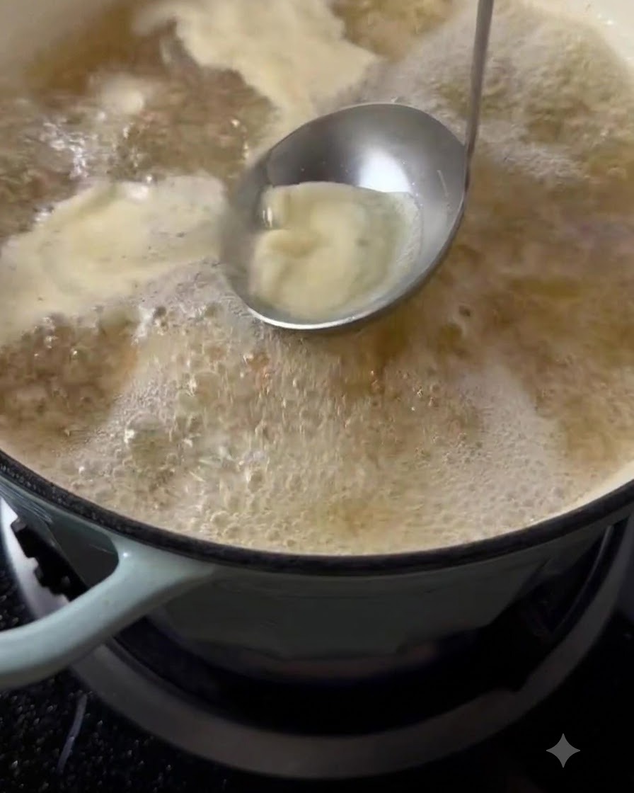Eine Metallkelle schöpft Schaum und Verunreinigungen von der kochenden Suppe ab.
