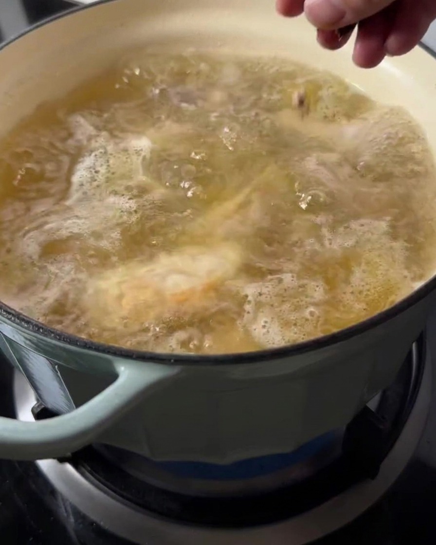 Eine Hand wirft rote Datteln in einen Topf mit simmernder Suppe.