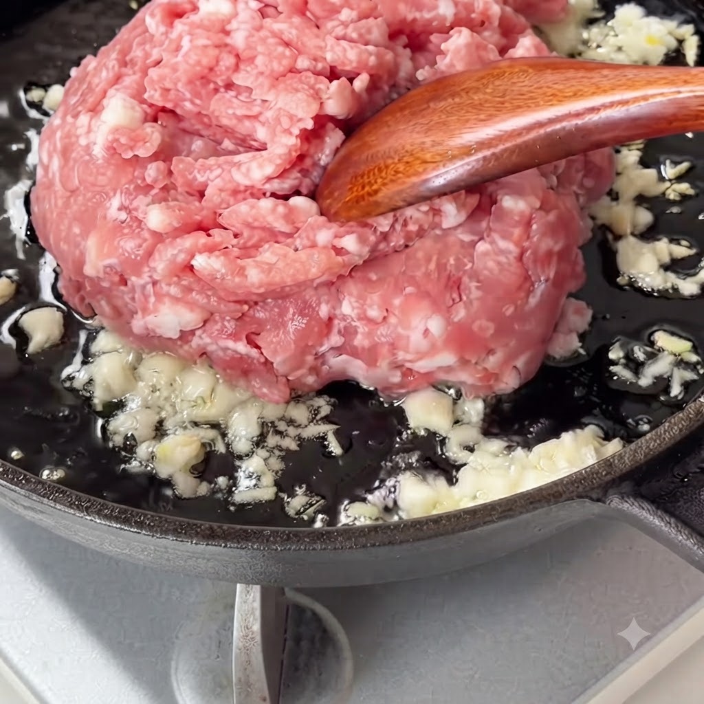 Rohes Schweinehackfleisch wird in eine Pfanne mit angebratenem Knoblauch gegeben.