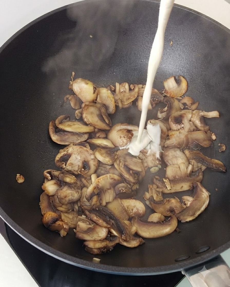 Sahne wird in eine Pfanne mit gebratenen Champignonscheiben gegossen.