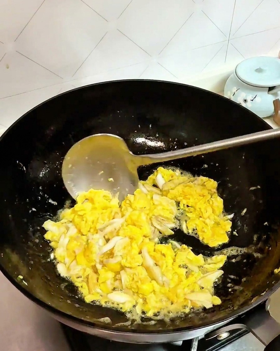 Krabbenfleisch und Eier werden zusammen in einem schwarzen Wok angebraten.